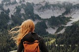Woman with backpack  looking out at snowy mountainscape.