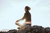 A woman meditating on the rocks