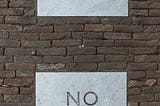 A brick wall with Yes and No written on two blank paper pieces.