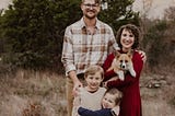 Husband and wife standing outside with their corgi dog and two sons