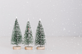 Three artificial Christmas trees covered in snow with snowflakes falling