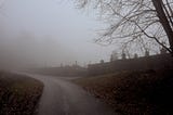 Road leading to a graveyard wall. Suitably atmospheric fog is present.