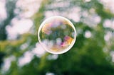 A large soap bubble floating in the air with a green foliage background