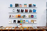 A wall mounted bookshelf featuring 4 shelves with 6 books on each. Minimalist and colorful.