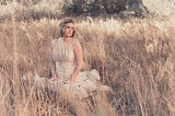 Female bride wearing a fancy gown sitting in the middle of wheat field, the wheat is as tall as she is.