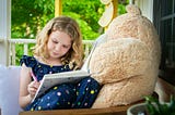 A young girl with a large teddy bear writing in a book