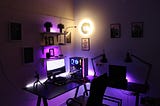 dark room lit by purple light of a desktop computer set up for editing youtube videos.