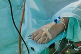 There’s a person on a hospital bed. They have an IV an tubes connected.