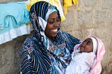 Miza Juma Juma, a new mom in Tanzania, smiles lovingly at her newborn baby, Umulayman, who she is cradling in her arms.