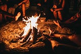 a bunch of people warming their hands and feet at a bonfire