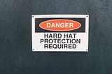 A sign reading “DANGER HARD HAT PROTECTION REQUIRED”