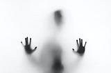 A dark figure against a white background. Only the outline of the head and hands is clearly visible, the rest is blurry.