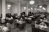 Black and White photograph from 1937 of the US Division of Classification and Cataloging. Long rows of desks with staff processing paperwork at each desk.