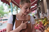 A woman holding a dragon fruit taps a white Ai Pin attached to her shirt.