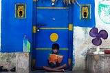 A little boy studying outside his home door.