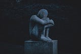 gray statue of a seated person holding their legs and hiding their face