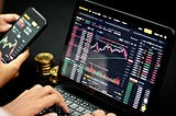 A picture of the a hand working on a computer system with the depiction of the crypto market on a screen.