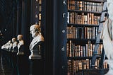 statues of ancient figures in front of bookshelves