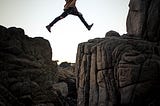 a girl is trying to jump from one rock to another