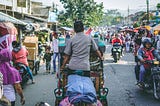 a busy street somewhere in Asia with people on mopeds and transporting lots of items on carts