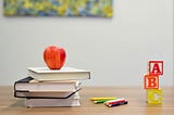 Books, pencils, letter blocks and an apple on a teacher’s desk.