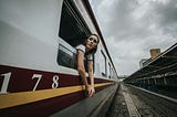 A woman hangs out of a passenger train, looking concerned.