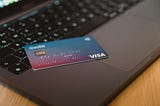 A Visa credit card sits on the edge of an open laptop.