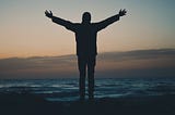 A man on the beach with hands held high.