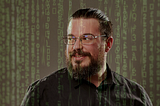 A portrait of a man (Justin) glancing over his shoulder. The Matrix-style green code is falling all around him.