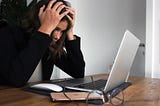 A woman with head in palms staring at a laptop screen