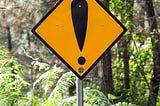Yellow warning sign on a post with no words on it, only a large black exclamation mark.