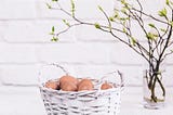 a basket of eggs beside a vase of sprouting branches