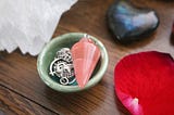 this is a photo of some crystals including a pink pendulum in a bowl.