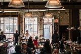Busy restaurant interior with diners eating and staff moving between tables.
