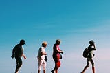 A group of elderly people walk ing. It seems like they are on the beach under a cloudless sky.