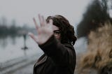 A woman standing in front of a street holds her palm up in front of her face.