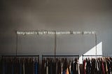 Neon lights above a clothing rack that reads: being naked is the #1 most sustainable option. we’re #2.