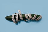 A measuring tape is wrapped around a cucumber.