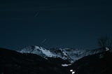 Snowy mountains at night with stars shooting across the sky.