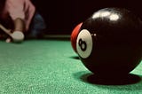 8 ball in the foreground, a person lining up to shoot the cue ball in the background