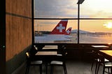 photo of tables in an airport, in front of a window overlooking plane tails