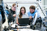 Three physical product designers working with the mechanical skeleton of a car.