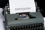 An antique typewriting with a sheet of paper that says, “Psychology”, sits on a table.