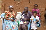 A religious leaders sits with a woman and two small children outside