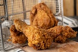 Fried chicken spilling out of fryer basket onto a table.