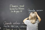 A child writes in chalk on a blackboard, in English and Portuguese