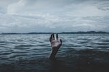 Image shows the hand of a drowning person waving to be saved from deep water, with a stormy overcast sky in the background.