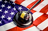 A black gavel with a gold band lies on an American flag