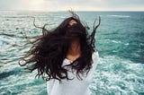 A woman with brown hair flying in the air while she stands in the midle of the sea (Do not ask me how)