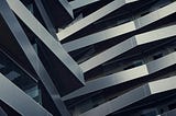 Close-up of a modern building façade with layered, angular metal panels forming a repeating geometric pattern.
